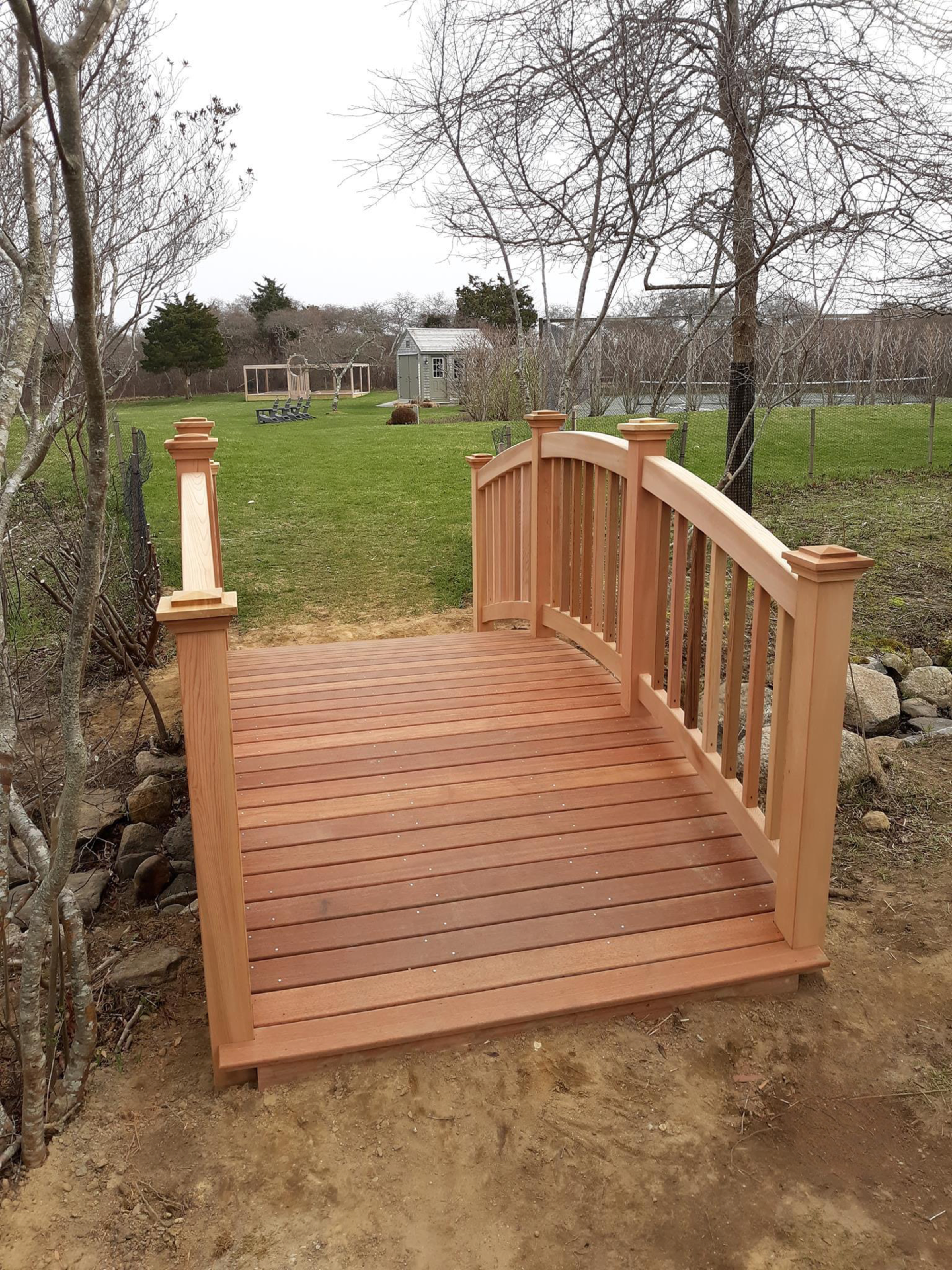 A custom-built wooden walkway in a Nantucket backyard. It is going over a small waterway and is constructed entirely of wood.