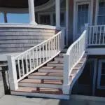 Curved exterior stair with white railings and mahogany treads rising to a shingled porch