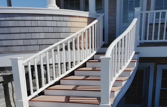 Curved exterior stair with white railings and mahogany treads rising to a shingled porch