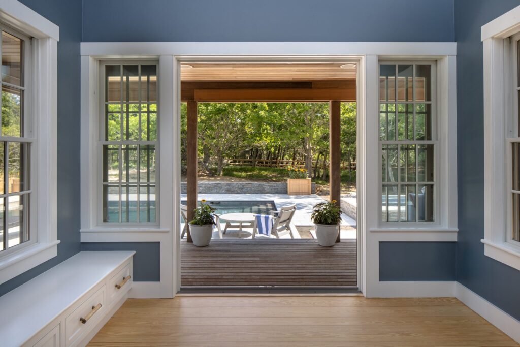 Blue sunroom with white window casings, custom storage bench, and open doors to the pool deck