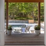 Open doors framing a slatted wood pool deck with planters and a stone retaining wall