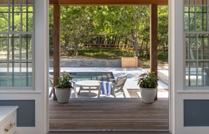 Open doors framing a slatted wood pool deck with planters and a stone retaining wall
