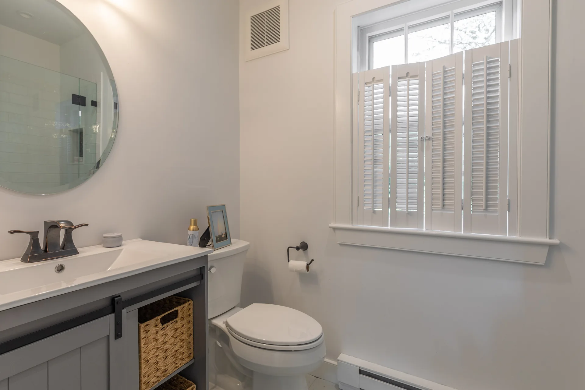 Bathroom with gray vanity, round mirror, and shutters